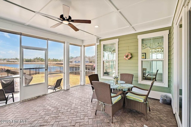 sunroom / solarium featuring a water view, a ceiling fan, a wealth of natural light, and brick floor