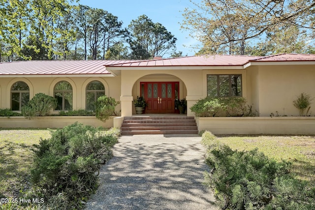 entrance to property with covered porch, stucco siding, and metal roof