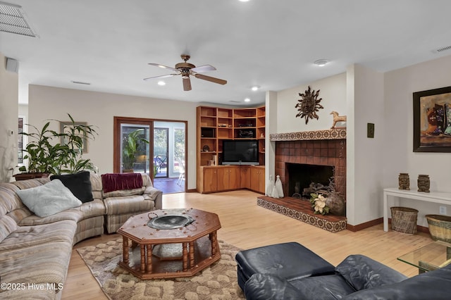 living room with light wood finished floors, a fireplace with raised hearth, ceiling fan, and visible vents