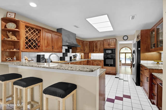 kitchen featuring open shelves, a peninsula, exhaust hood, black appliances, and decorative backsplash