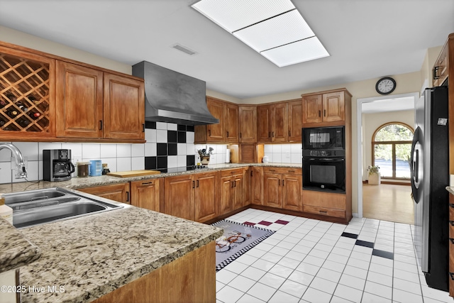 kitchen featuring backsplash, a sink, wall chimney range hood, visible vents, and black appliances