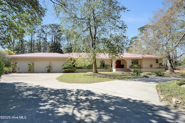 ranch-style home featuring metal roof, stucco siding, an attached garage, and concrete driveway
