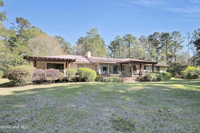 ranch-style house with a chimney, a front yard, stucco siding, and metal roof