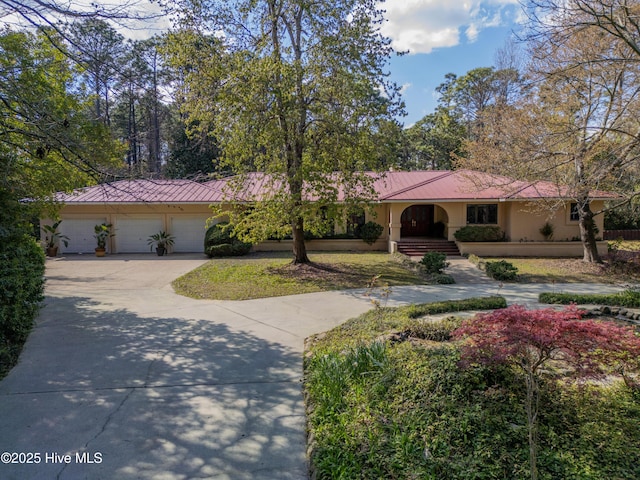 ranch-style house featuring metal roof, an attached garage, concrete driveway, a standing seam roof, and stucco siding