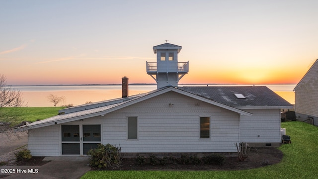 back of house featuring a lawn, a shingled roof, and a water view