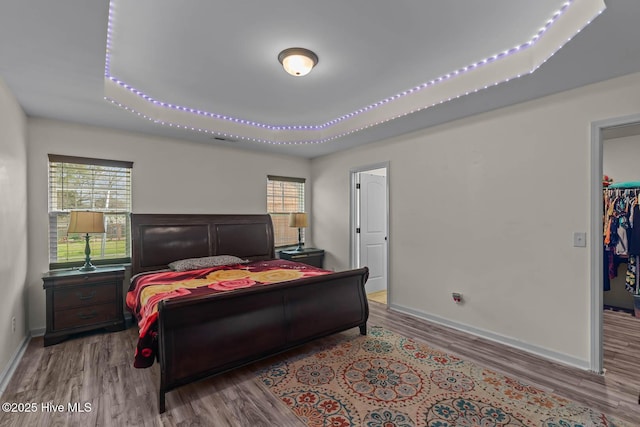 bedroom with baseboards, wood finished floors, and a walk in closet