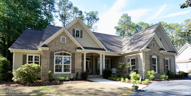 craftsman-style home with a porch, a shingled roof, and stone siding