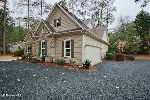 view of home's exterior with stone siding, a shingled roof, an attached garage, and aphalt driveway