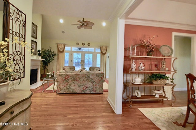 living area with wood finished floors, a ceiling fan, a fireplace, and crown molding