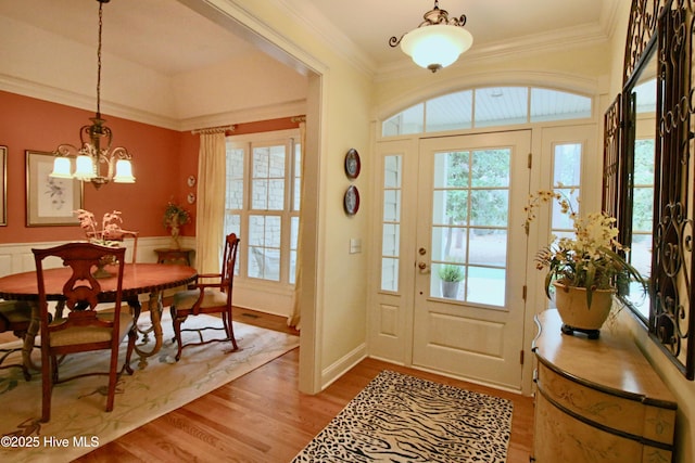 entryway featuring crown molding, a wainscoted wall, a notable chandelier, and wood finished floors