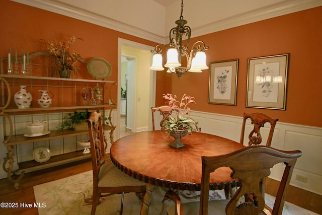 dining space featuring ornamental molding, a chandelier, wainscoting, and wood finished floors