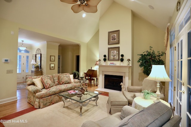 living room with wood finished floors, baseboards, high vaulted ceiling, a ceiling fan, and a fireplace with flush hearth