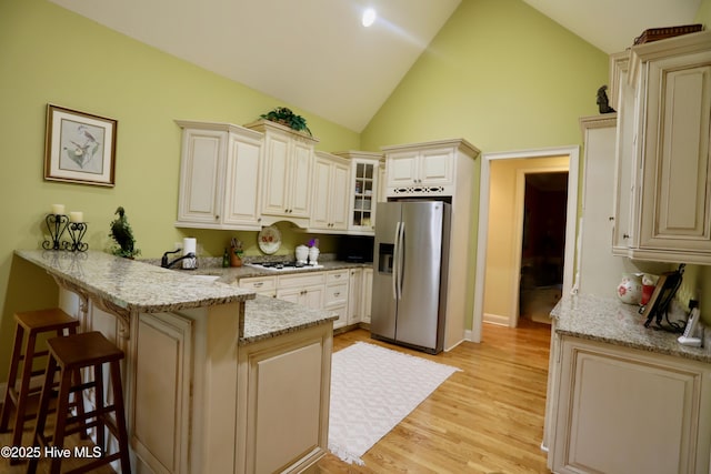 kitchen with a breakfast bar area, glass insert cabinets, light wood-style floors, a peninsula, and stainless steel fridge with ice dispenser