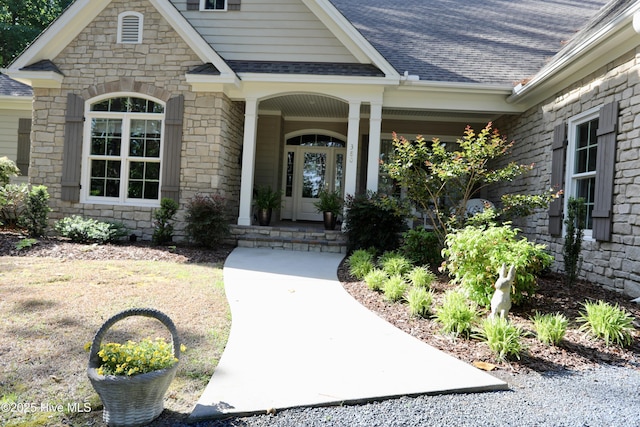 doorway to property with covered porch, a shingled roof, and stone siding
