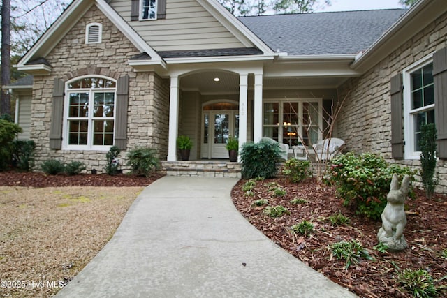 property entrance featuring a porch, stone siding, and roof with shingles