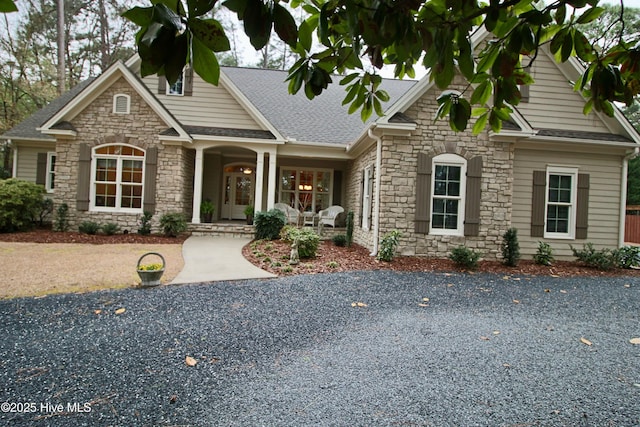 craftsman-style house with stone siding, covered porch, and roof with shingles