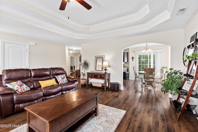 living area with a raised ceiling, dark wood finished floors, ceiling fan with notable chandelier, visible vents, and arched walkways