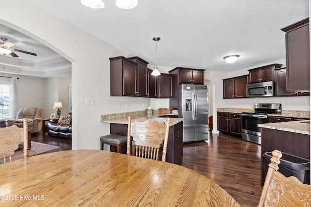 kitchen featuring arched walkways, dark wood-style floors, ceiling fan, dark brown cabinetry, and appliances with stainless steel finishes