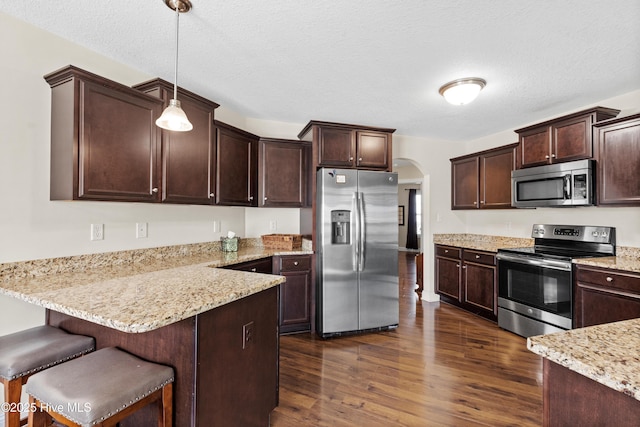 kitchen with dark wood-type flooring, arched walkways, a peninsula, dark brown cabinets, and appliances with stainless steel finishes