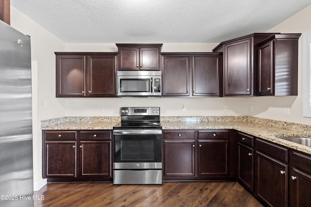 kitchen featuring dark wood finished floors, light stone counters, dark brown cabinets, and stainless steel appliances