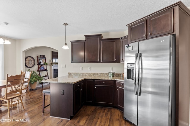 kitchen with a peninsula, stainless steel fridge with ice dispenser, dark brown cabinetry, and dark wood finished floors