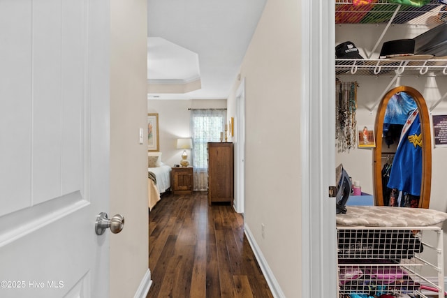 corridor featuring baseboards, ornamental molding, a raised ceiling, and hardwood / wood-style flooring