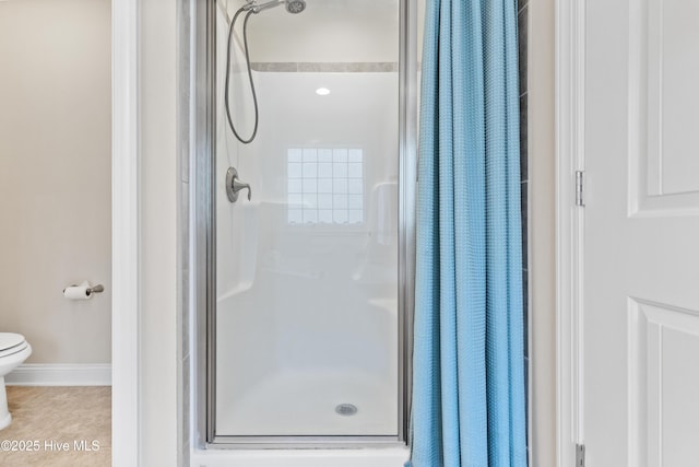 bathroom featuring toilet, a stall shower, tile patterned flooring, and baseboards