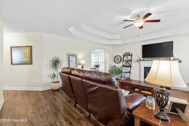 living room featuring a fireplace, wood finished floors, a ceiling fan, a raised ceiling, and arched walkways
