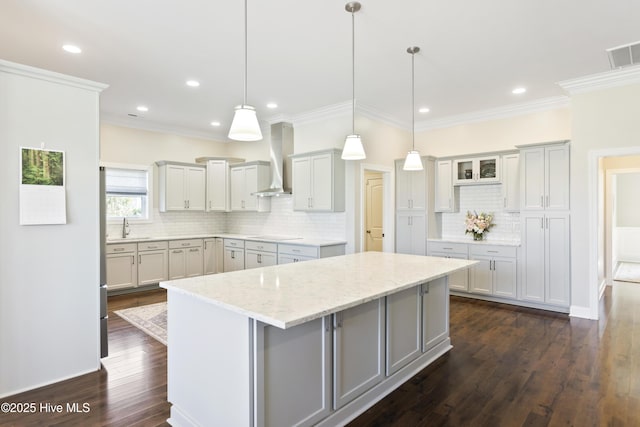 kitchen featuring dark wood-style flooring, visible vents, wall chimney exhaust hood, a sink, and a center island