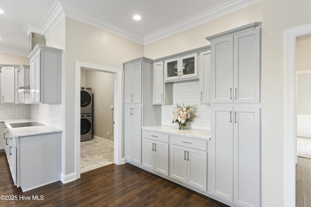 kitchen featuring gray cabinetry, black electric cooktop, dark wood-style flooring, crown molding, and stacked washer and dryer
