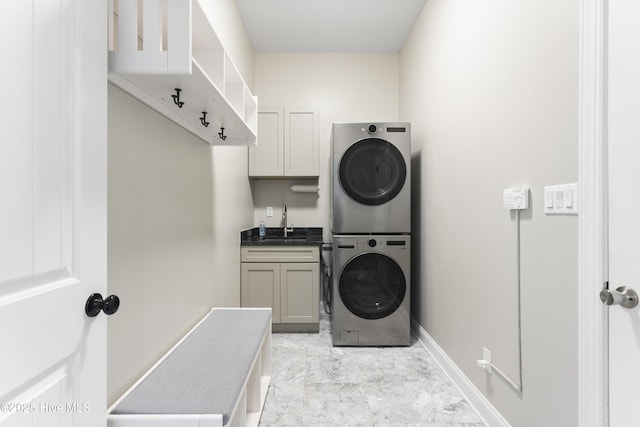 washroom with a sink, cabinet space, baseboards, and stacked washer / drying machine