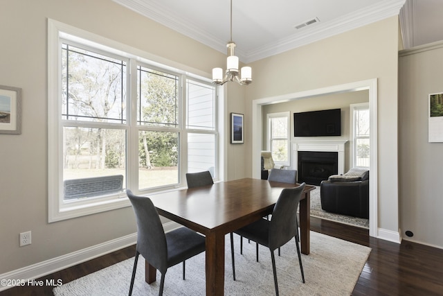 dining space with baseboards, a fireplace, ornamental molding, dark wood finished floors, and a notable chandelier