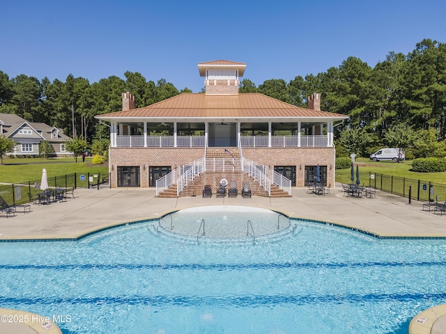 community pool with a patio, stairs, fence, and a lawn
