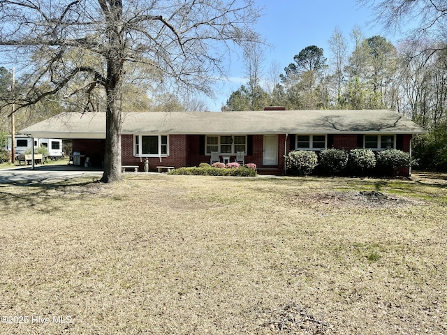 ranch-style house with a front yard, brick siding, a chimney, driveway, and an attached carport