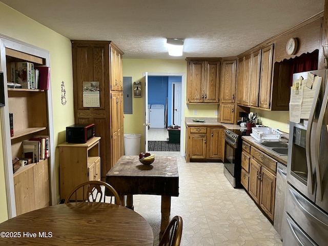 kitchen featuring washer / clothes dryer, electric panel, a sink, a textured ceiling, and stainless steel appliances