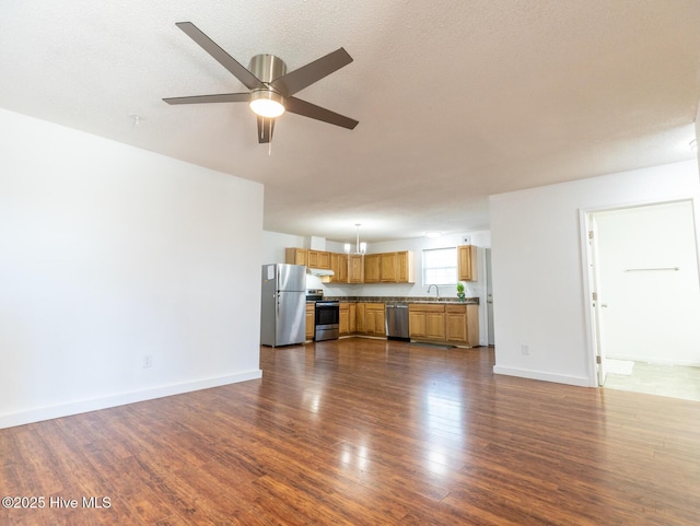 unfurnished living room with dark wood finished floors, baseboards, ceiling fan, and a sink