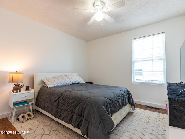 bedroom with baseboards, a textured ceiling, visible vents, a ceiling fan, and wood finished floors