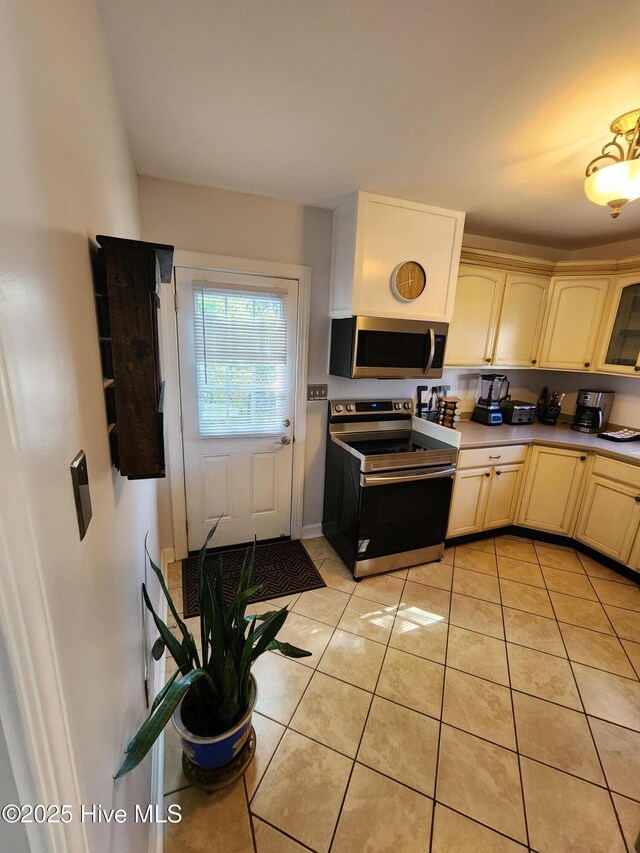 kitchen featuring light tile patterned flooring, light countertops, cream cabinetry, and appliances with stainless steel finishes