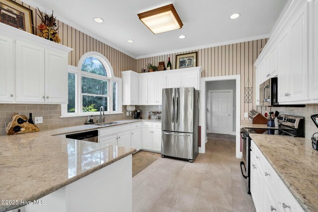kitchen featuring white cabinetry, wallpapered walls, a sink, light stone countertops, and appliances with stainless steel finishes