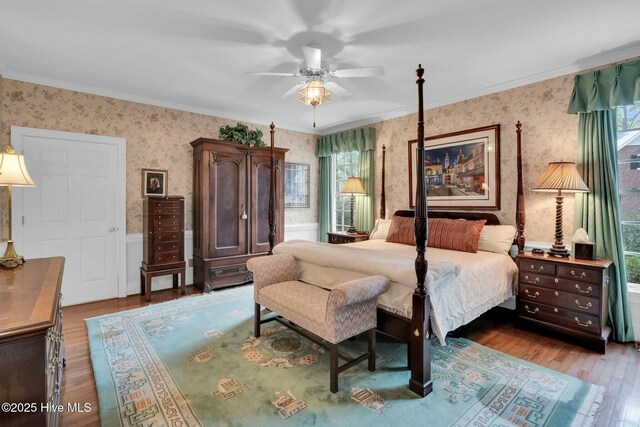 bedroom featuring wallpapered walls, wood finished floors, crown molding, and wainscoting
