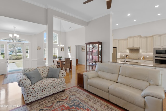 living area with crown molding, recessed lighting, light wood-style floors, ceiling fan with notable chandelier, and a high ceiling