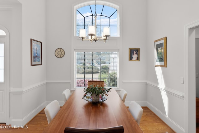 dining room featuring baseboards, wood finished floors, a towering ceiling, and a chandelier