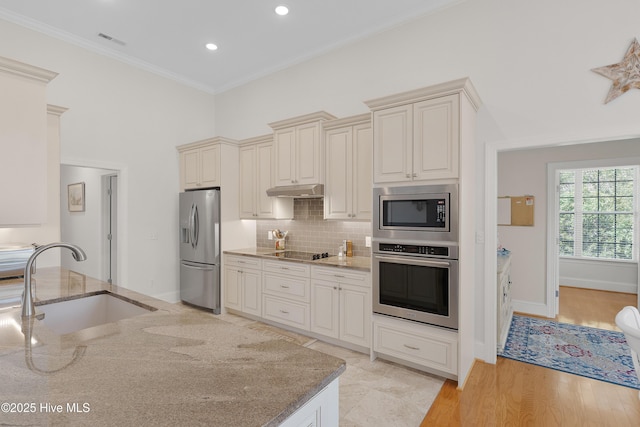 kitchen featuring stainless steel appliances, cream cabinetry, a sink, light stone counters, and visible vents