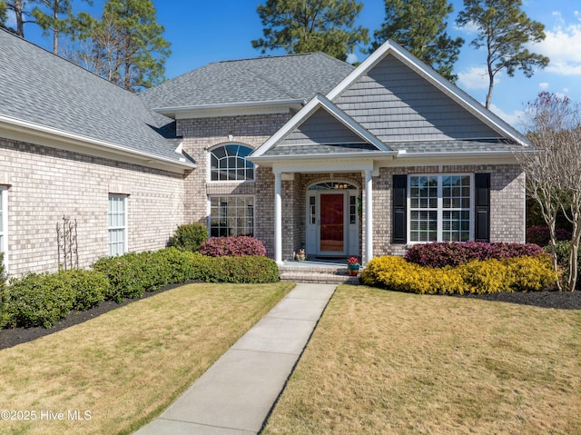 view of front of property featuring brick siding, a front yard, and roof with shingles