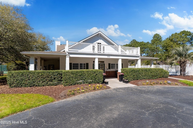 view of front of property with a balcony, fence, a chimney, brick siding, and a porch