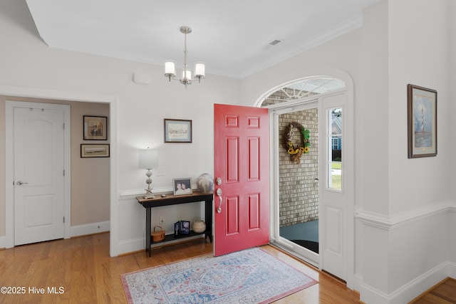 foyer entrance with baseboards, visible vents, wood finished floors, and an inviting chandelier