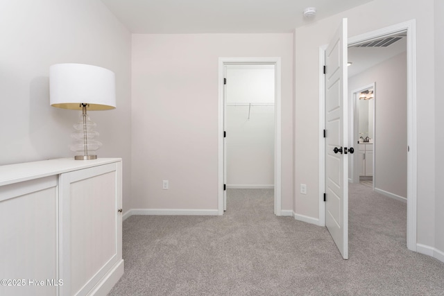 unfurnished bedroom featuring light carpet, baseboards, visible vents, and a walk in closet