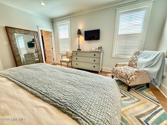 bedroom with wood finished floors, crown molding, a walk in closet, and baseboards