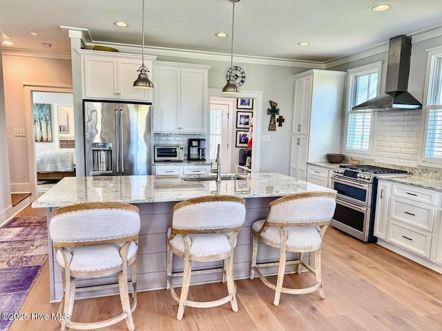 kitchen featuring stainless steel appliances, backsplash, a sink, white cabinetry, and wall chimney exhaust hood