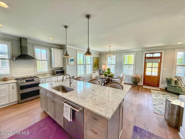 kitchen with light wood finished floors, a sink, wall chimney range hood, ornamental molding, and appliances with stainless steel finishes
